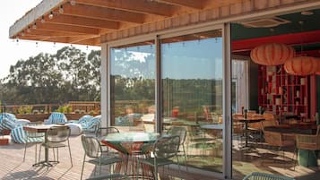 Un patio exterior con puertas de vidrio, muebles de mimbre y vistas del paisaje circundante.