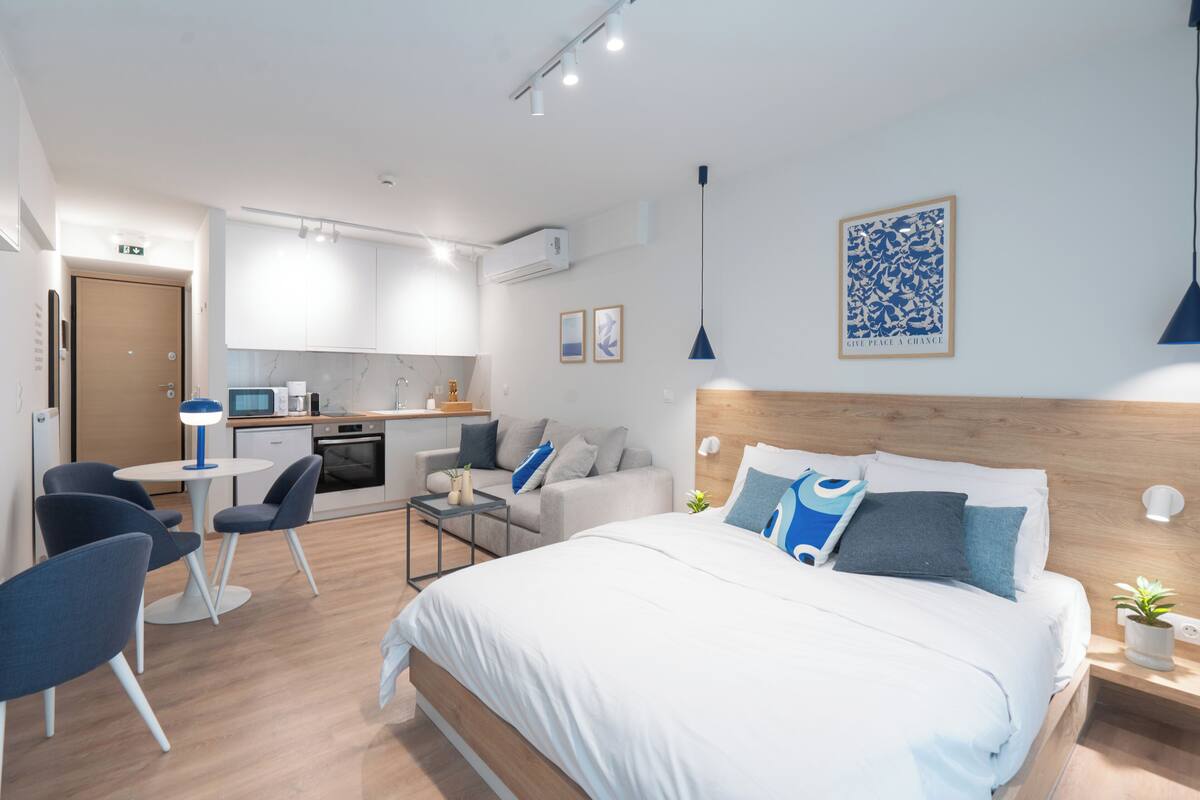A modern hotel room with a bed, a desk, a chair, and a kitchenette.