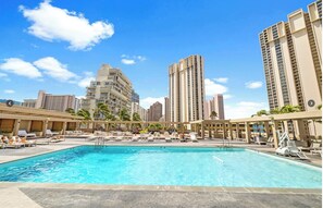 Una piscina con sillones de descanso y sombrillas, rodeada de edificios altos.