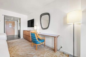 Habitación de hotel con cama, escritorio, silla, televisor de pantalla plana, espejo y lámpara.