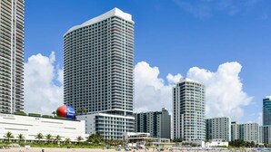 Un hotel sulla spiaggia con diversi edifici a grattacielo, un cielo azzurro e una spiaggia sabbiosa con persone.