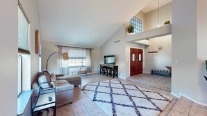 Ein geräumiges Wohnzimmer mit einer Couch, einem Couchtisch und einem Fernseher. Eine Treppe führt zu einer oberen Ebene mit einem Balkon.