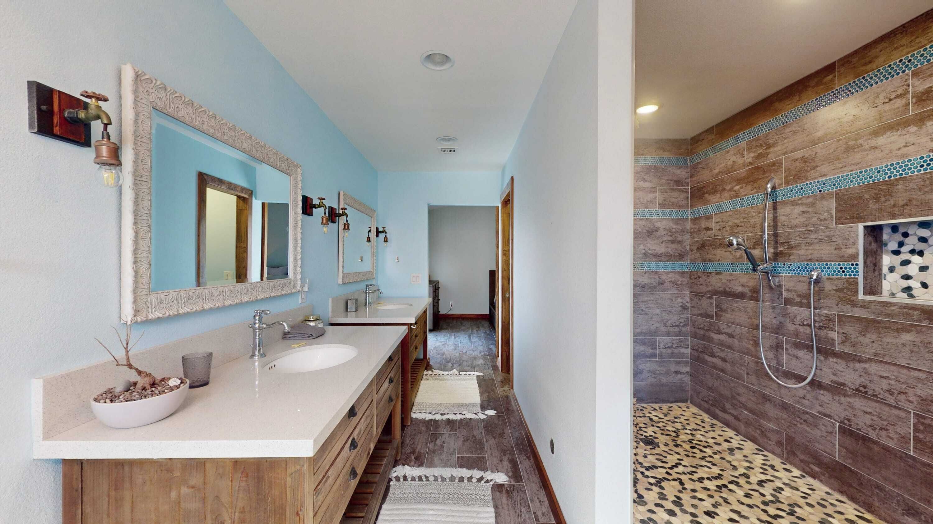 A bathroom with a double sink vanity, a mirror, and a shower area with a wooden wall and mosaic tiles.