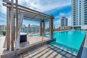 Une piscine sur le toit, agrémentée d’une pergola, de chaises longues et offrant une vue sur le paysage urbain.