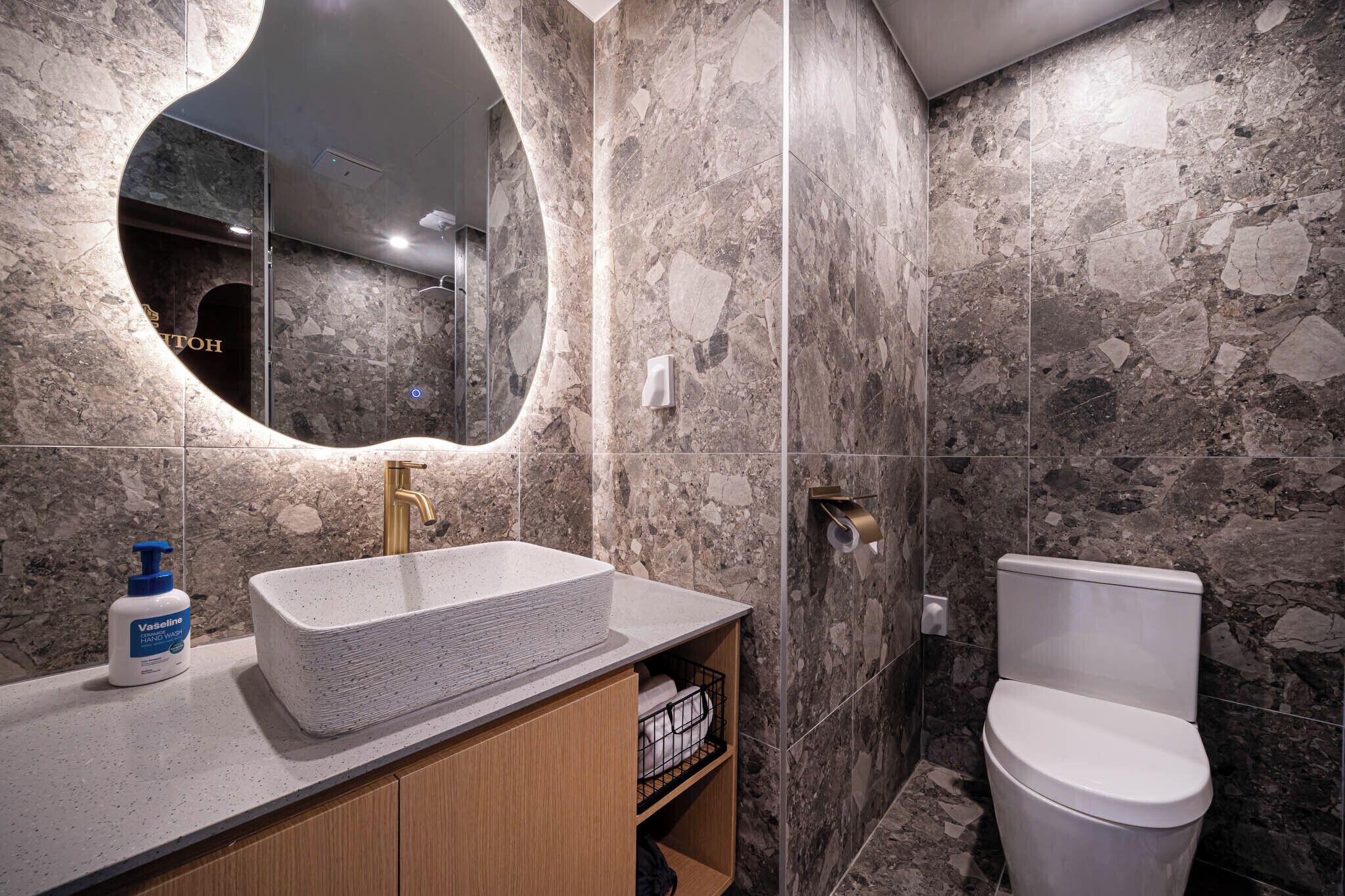 A bathroom with a stone wall, a sink with a soap dispenser, and a toilet.