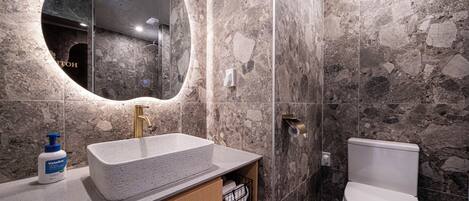 A bathroom with a stone wall, a sink with a soap dispenser, and a toilet.