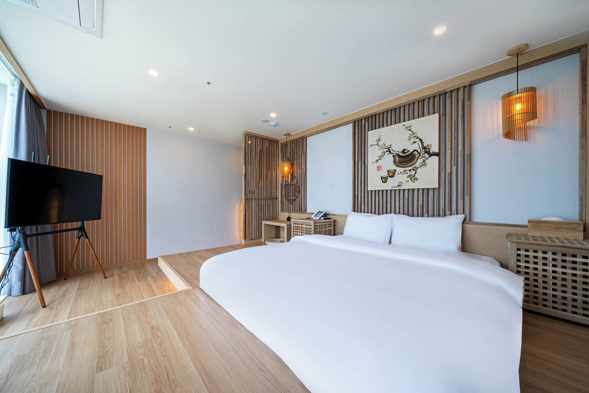 Une chambre d’hôtel moderne avec un grand lit, un téléviseur posé sur un meuble, un petit bureau et une œuvre d’art accrochée au mur.