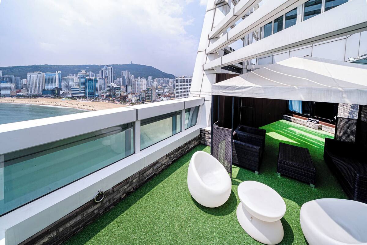 Terraza en la azotea con vista a la ciudad, césped artificial verde y mobiliario exterior.
