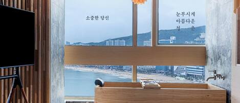 A modern hotel room with a large window, wooden panel wall, and a wooden vanity with a sink.