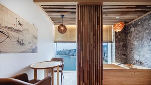 A modern interior with a wooden partition, a round table with chairs, a large window with a city view, and a stone wall.