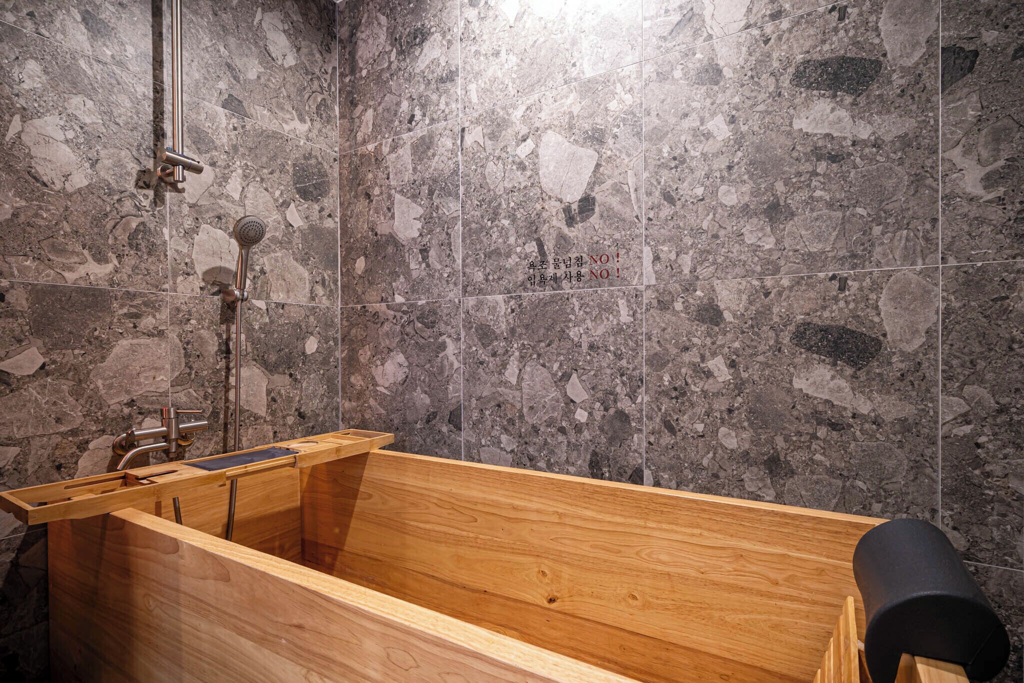 A wooden bathtub in a bathroom with a stone tile wall.