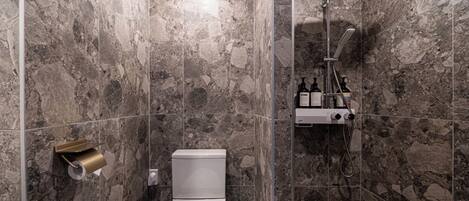Een moderne badkamer met een marmeren douche, een toilet en een handdroger.