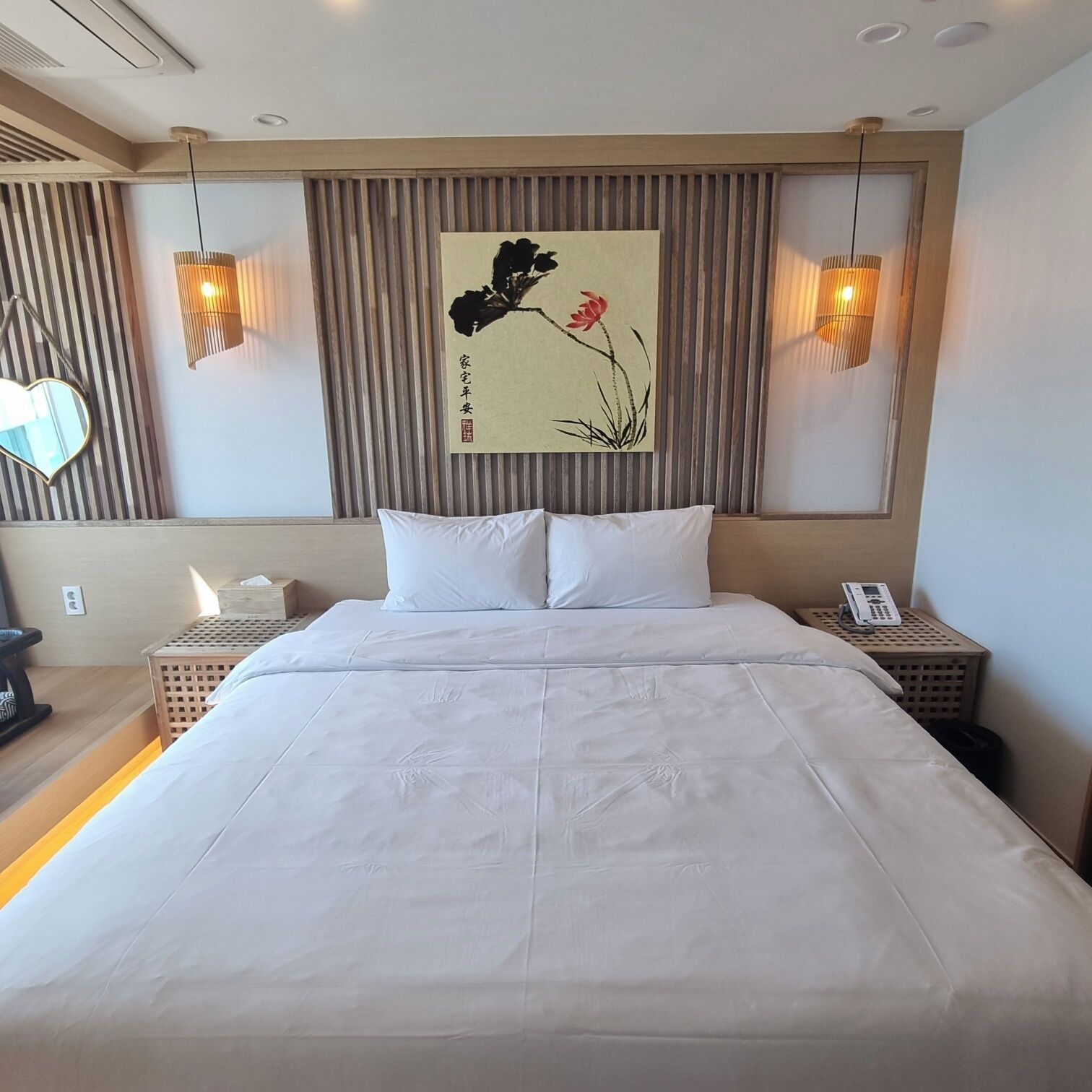 A hotel room with a large bed, two bedside tables, a wall-mounted artwork, and two wall sconces.
