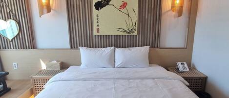 A hotel room with a large bed, two bedside tables, a wall-mounted artwork, and two wall sconces.