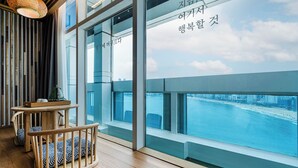 A modern interior with large windows overlooking a waterfront, wooden furniture, and a view of the cityscape.