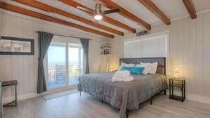 Ein Schlafzimmer mit Bett, Deckenventilator, einem Fenster mit Vorhängen und Blick ins Freie.