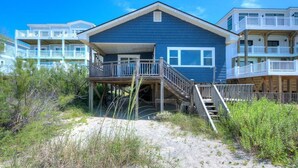 Ein Strandhaus mit Holzterrasse und Treppe zu einem Balkon.