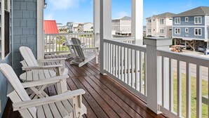 Une véranda couverte avec des fauteuils Adirondack blancs, une vue sur les maisons voisines et un ciel bleu dégagé.