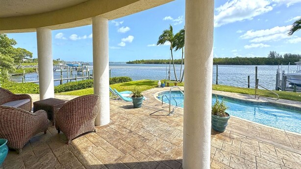 A covered outdoor area with a pool, lounge chairs, and a view of the marina and water. - Sandman's Haven Retreat (Stuart)