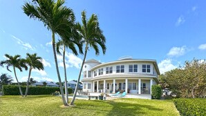 A large, two-story house with a curved roof, a swimming pool, and palm trees in the yard. - Sandman's Haven Retreat (Stuart)