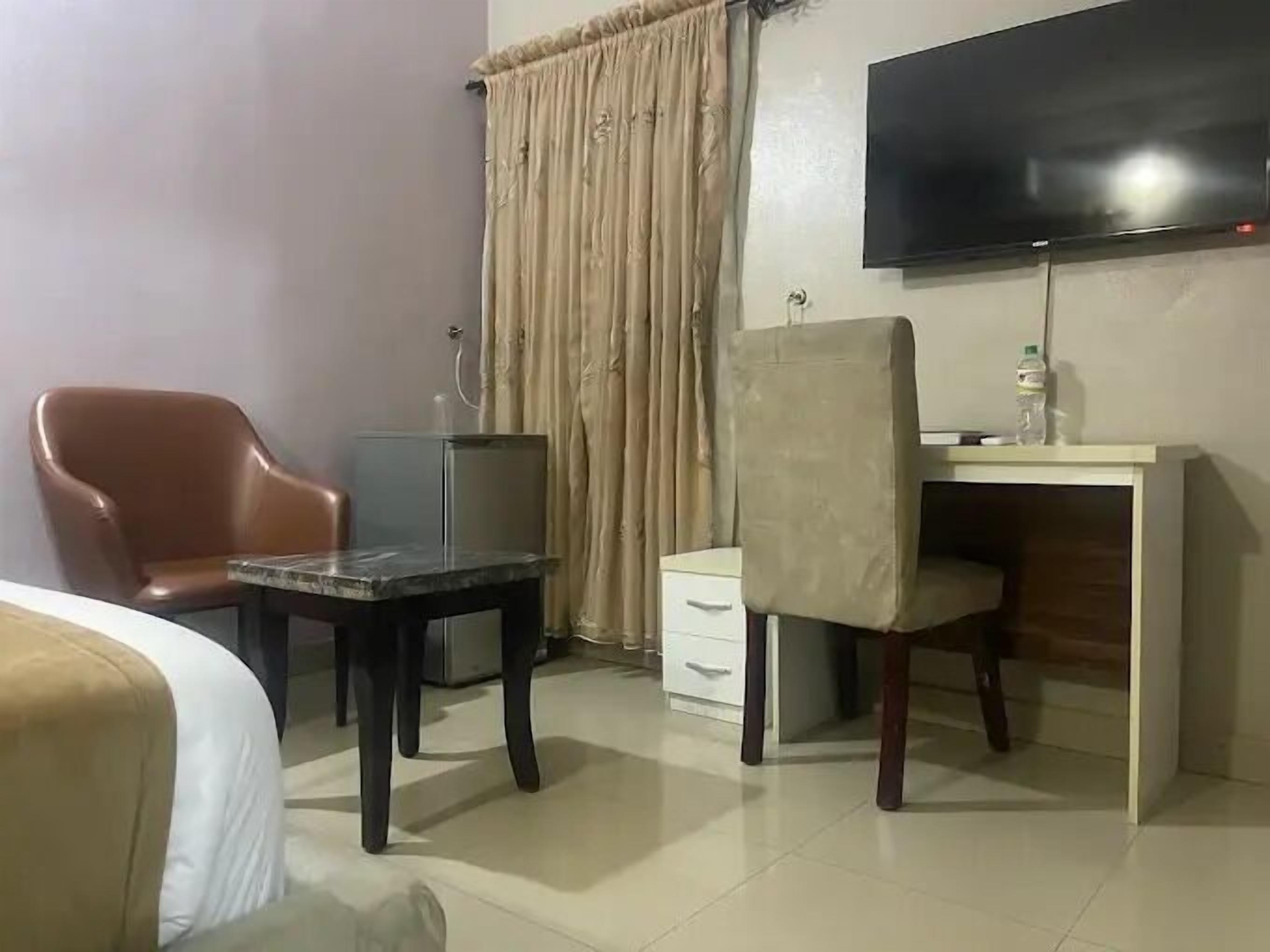 Una habitación de hotel con cama, escritorio, silla, televisor y cortina.