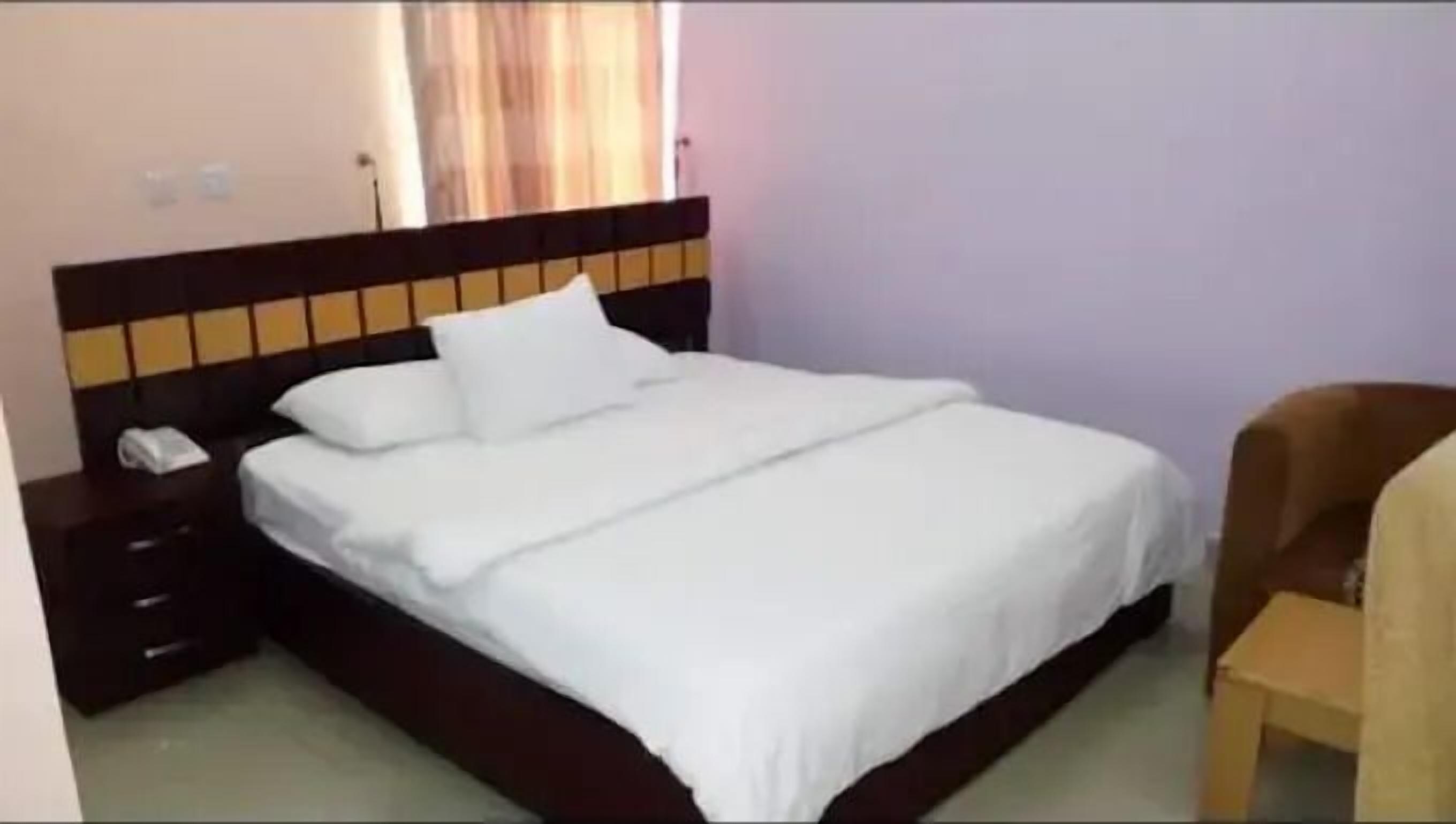 A neatly made bed with white linens in a room with a wooden headboard and a small bedside table.