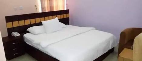 A neatly made bed with white linens in a room with a wooden headboard and a small bedside table.