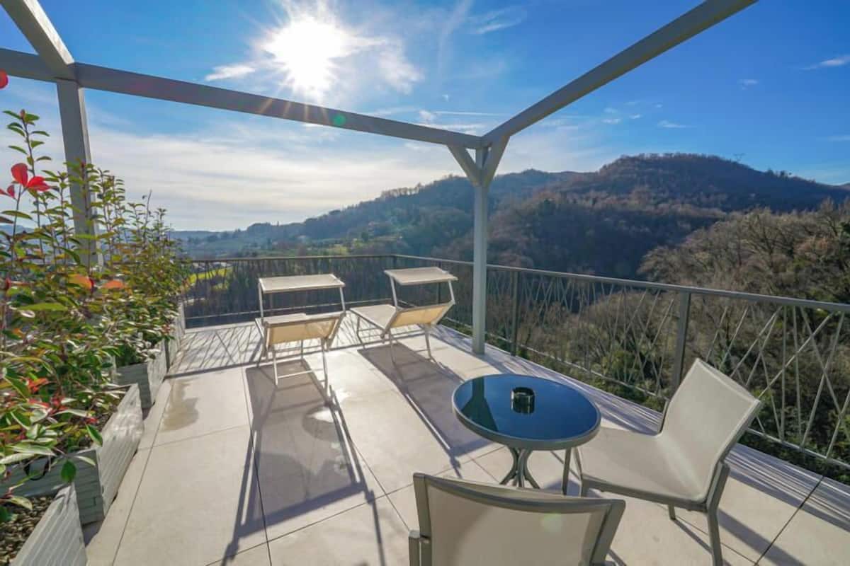 A balcony with a table and chairs, overlooking a mountainous landscape.