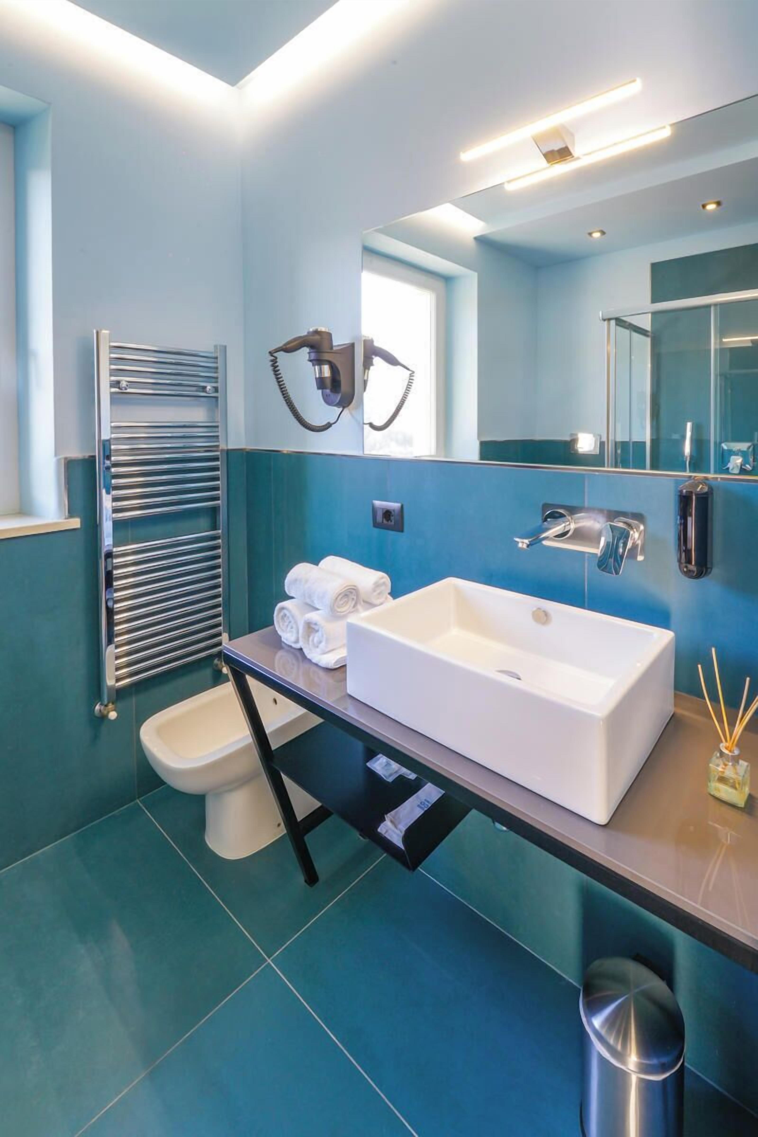 A modern bathroom with a white sink, a towel rack, a toilet, and a mirror.