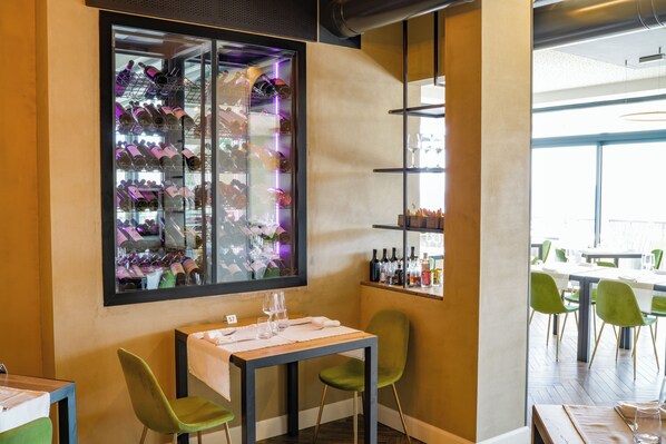 A restaurant interior with a wine display, green chairs, and a table set for two.