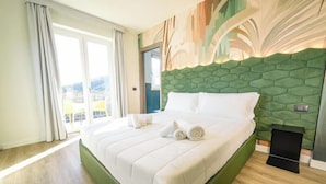 A hotel room with a large bed, a green headboard, and a view of the outdoors through a sliding door. - Hotel Vita (Salò)