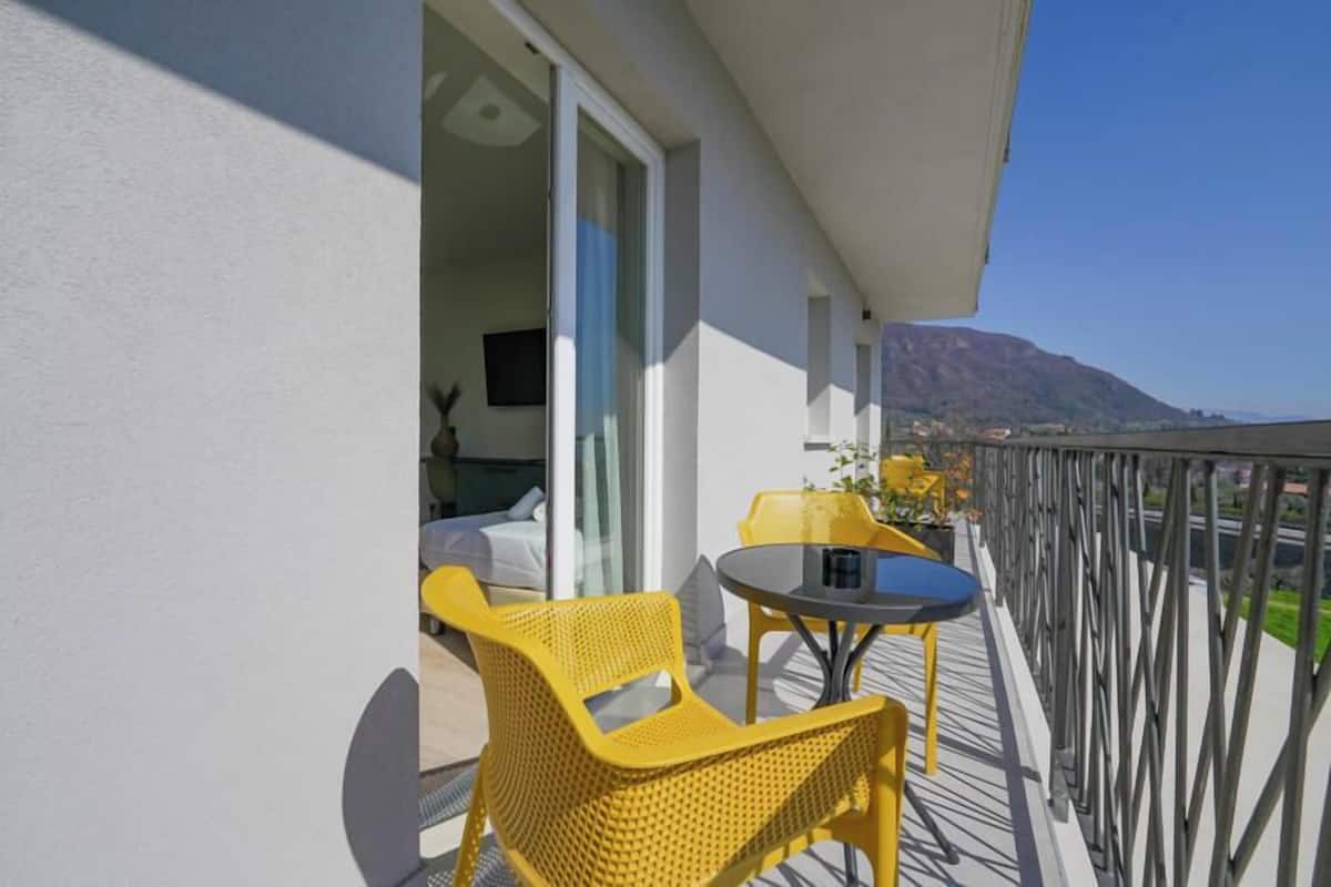 A balcony with yellow wicker chairs and a small table, overlooking a mountainous landscape.