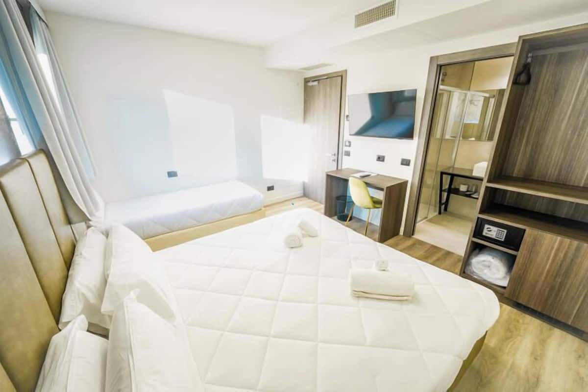 A hotel room with a large bed, a desk, a chair, a TV, and a wardrobe.