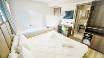 Habitación de hotel con una cama grande, un escritorio, una silla, un televisor y un armario.