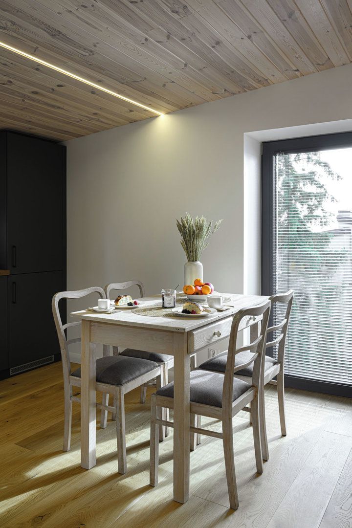 Un comedor con mesa de madera, sillas blancas y ventana con persianas.