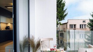 Un balcón moderno con puerta de cristal, una mesa de comedor con sillas y plantas en macetas.