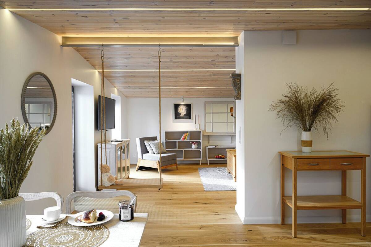 Una sala de estar moderna con techo de madera, un sofá, un televisor y un comedor con mesa y sillas.