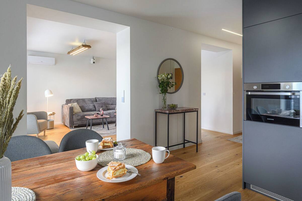 Una sala de estar moderna con una mesa de comedor de madera, un sofá y una zona de cocina con horno empotrado.