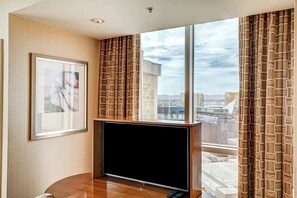 Une chambre d’hôtel moderne dotée d’une grande fenêtre, d’un téléviseur à écran plat, d’une œuvre d’art encadrée et de rideaux à motifs.