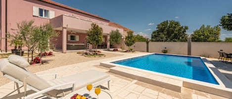 A swimming pool with lounge chairs and a table with fruit and drinks.