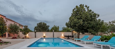 Ein Swimmingpool mit Liegestühlen und einer Obstschale auf einem Tisch.
