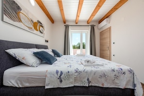 A bedroom with a bed, a painting, a window, and a door.
