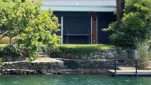 Ein modernes, zweistöckiges Gebäude mit Balkon, umgeben von üppiger Vegetation und freiem Blick auf das Wasser.