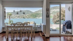 Ein Essbereich mit Seeblick und Hügeln, ein Grill draußen und ein helles Interieur.