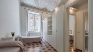 Ein Schlafzimmer mit Bett, Fenster, Heizkörper und einem Flur mit gemustertem Boden.