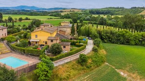 A villa with a swimming pool, surrounded by lush greenery and fields.