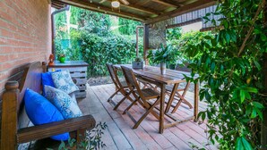 A covered patio with wooden furniture, a ceiling fan, and potted plants.