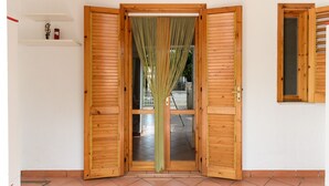 Une porte en bois avec un rideau vert, une petite étagère sur laquelle est posé un vase, et une fenêtre avec des volets en bois.