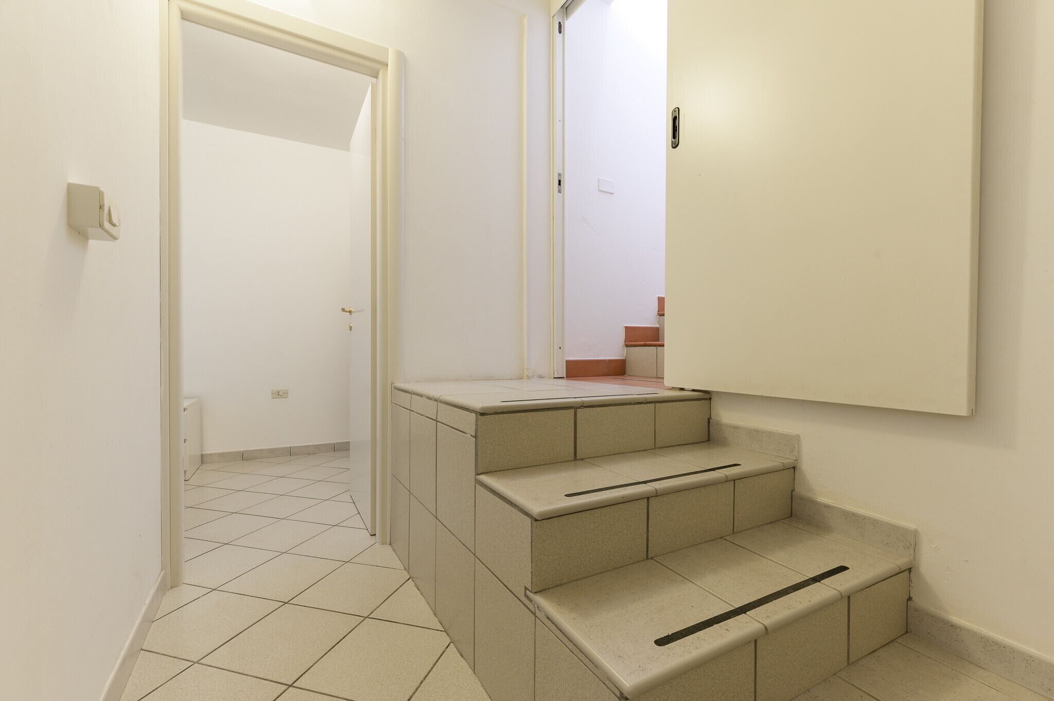 A hallway with a tiled floor, a set of beige steps, and a white door.