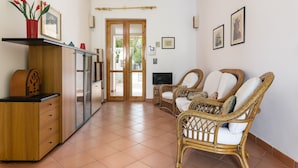 Une pièce avec un meuble en bois, un téléviseur, des chaises en osier et une porte donnant sur l’extérieur.